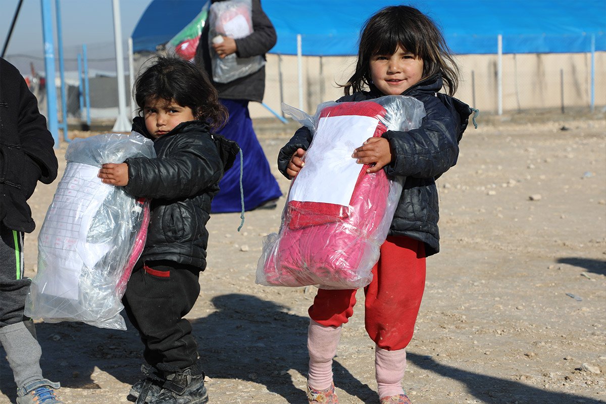 Zwei kleine Mädchen halten Winterkleidung von Help in der Hand