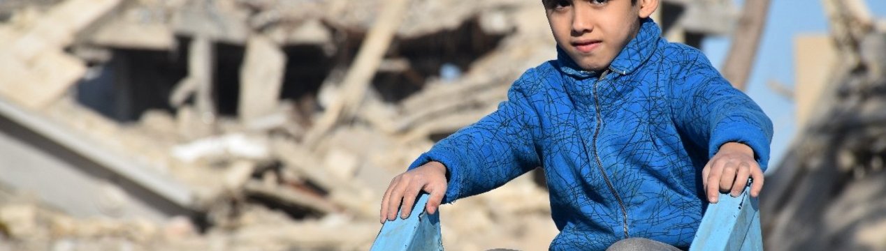 Syrischer Junge auf Rutsche vor zerstörtem Gebäude